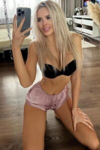Dasha taking a mirror selfie in black bra and pink shorts, blonde escort in Amsterdam